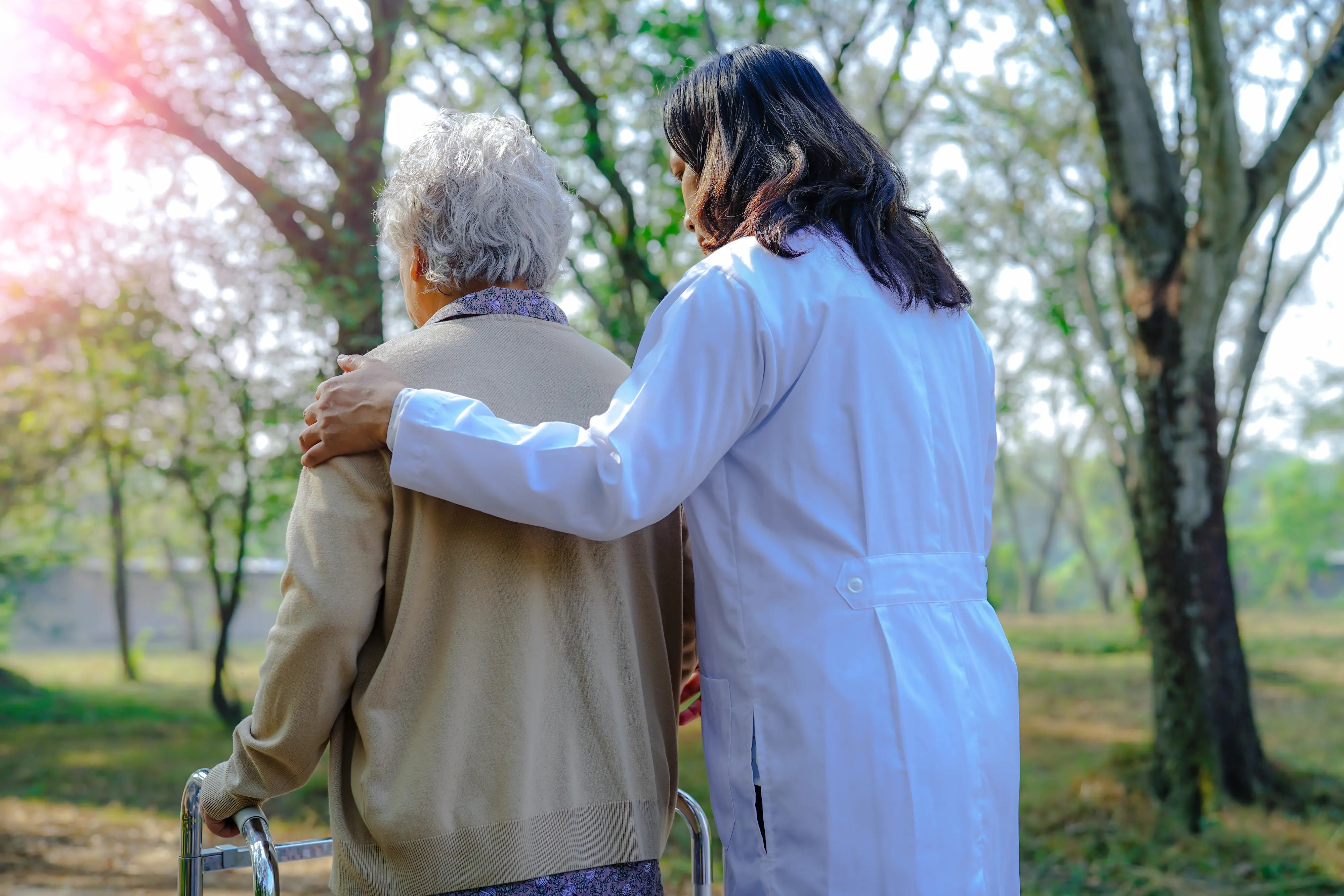 Healthcare worker supporting an elderly woman using a walker during outdoor rehabilitation walk in a park setting