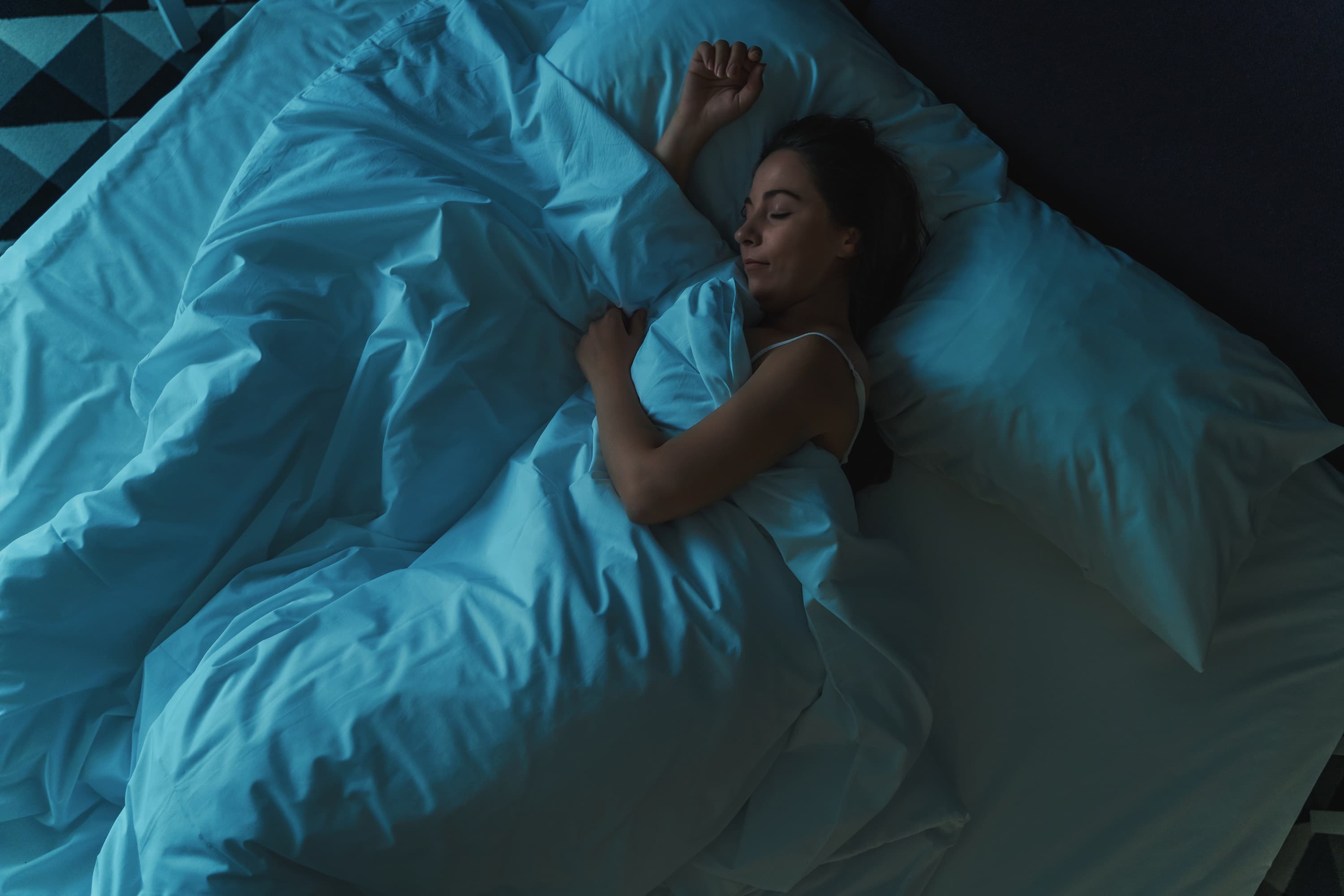 Woman sleeping peacefully in a cool blue-lit bedroom, illustrating the connection between sleep temperature regulation and quality rest