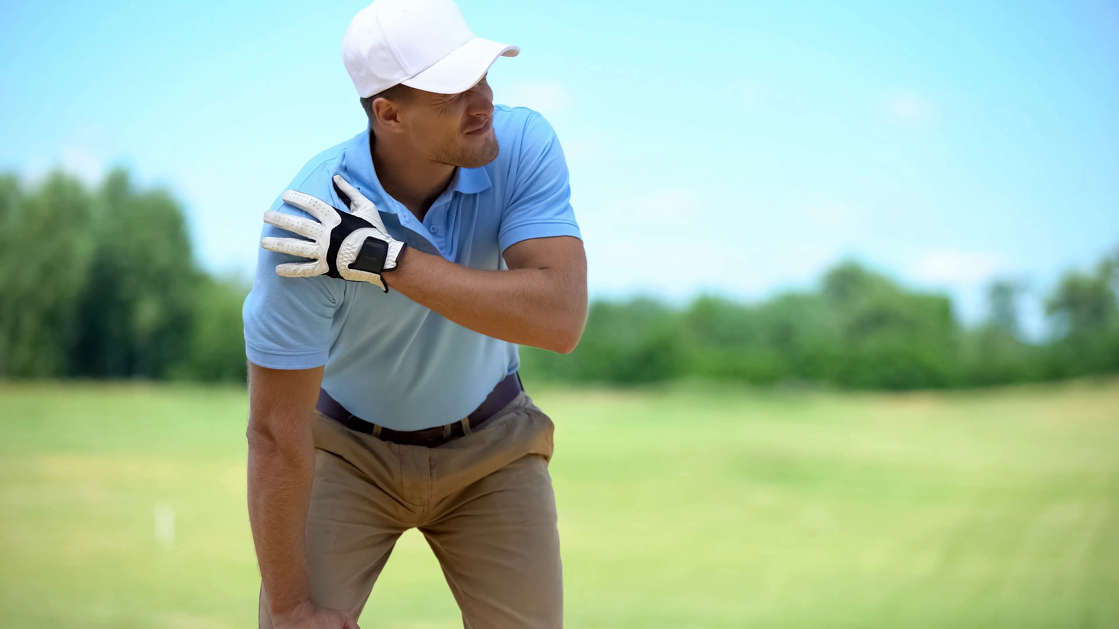 Male golfer holding his shoulder in pain on a golf course during a swing, suggesting a sports-related shoulder injury.