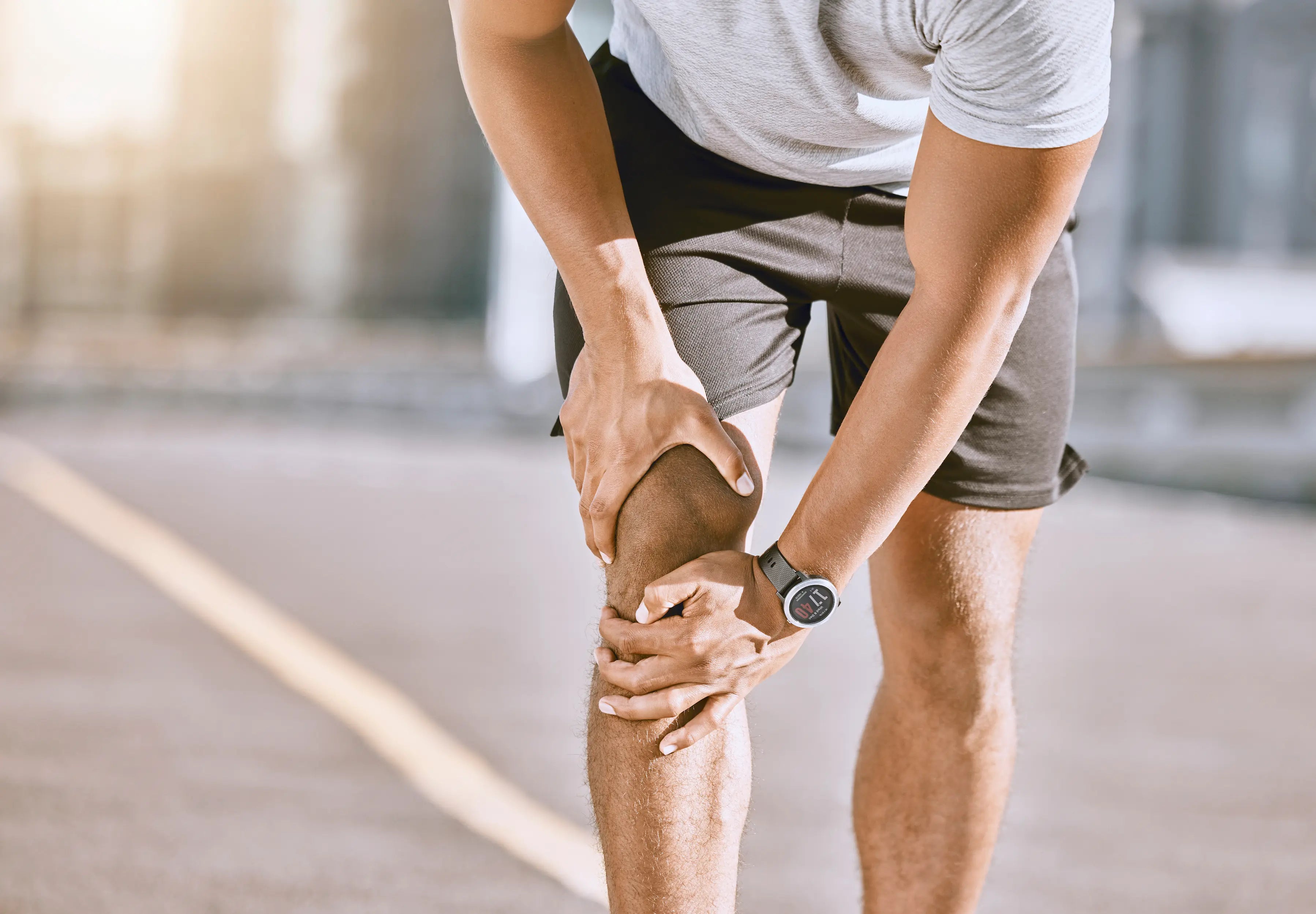 Person holding their knee in pain after a sports injury, suggesting a possible ligament strain while exercising outdoors.