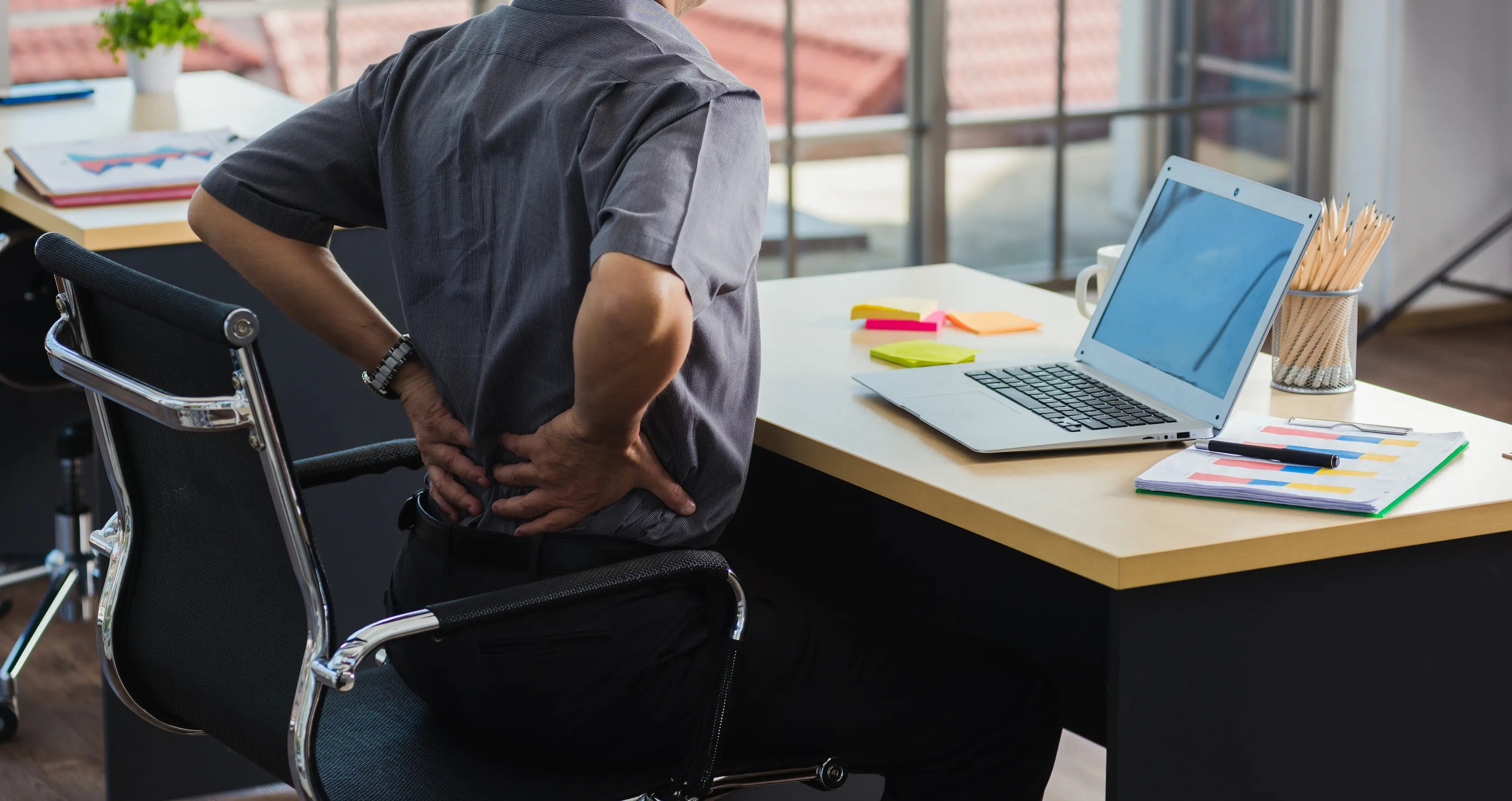 Person sitting at a desk holding their lower back in pain, illustrating the need for cold therapy relief for lower back pain