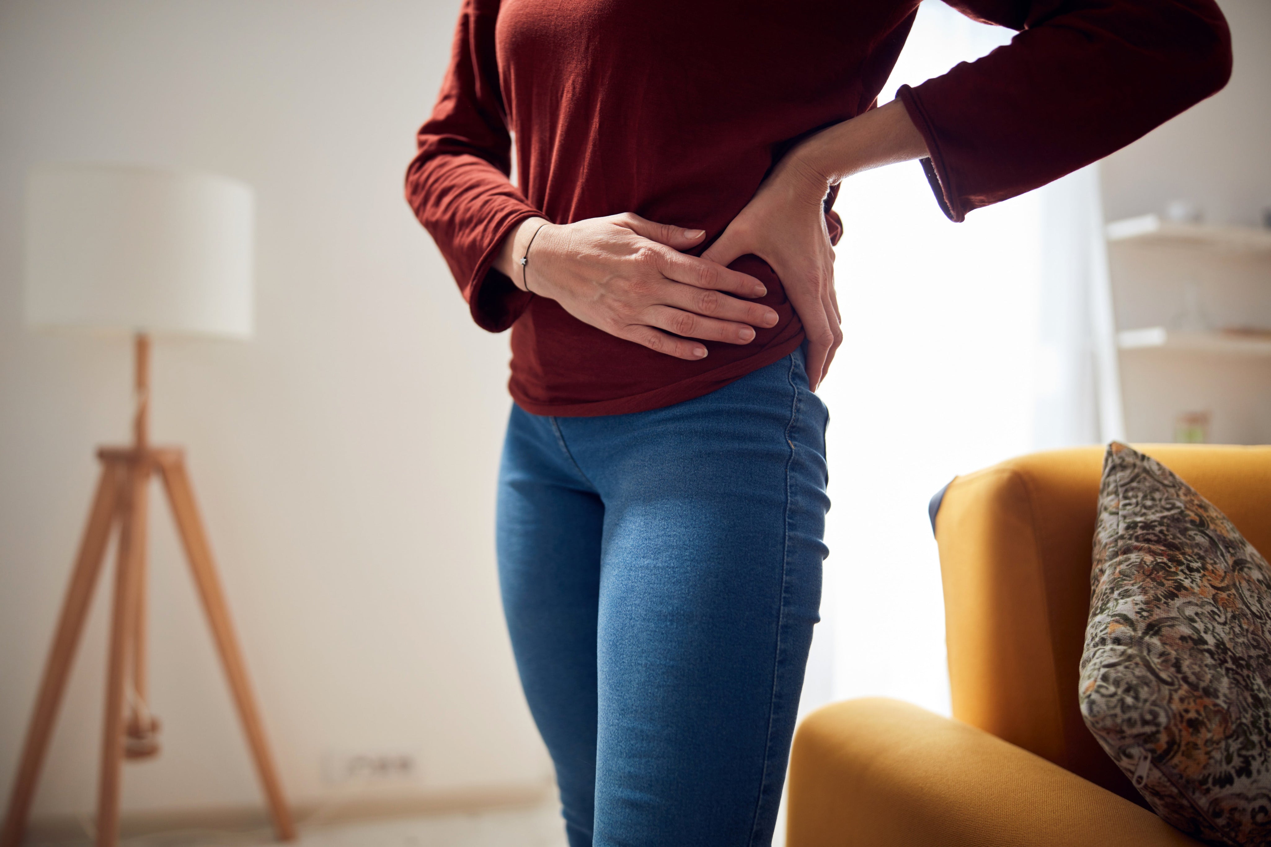 A woman holding the side of her hip while standing, showing discomfort commonly associated with menopause-related hip pain or gluteal tendinopathy.