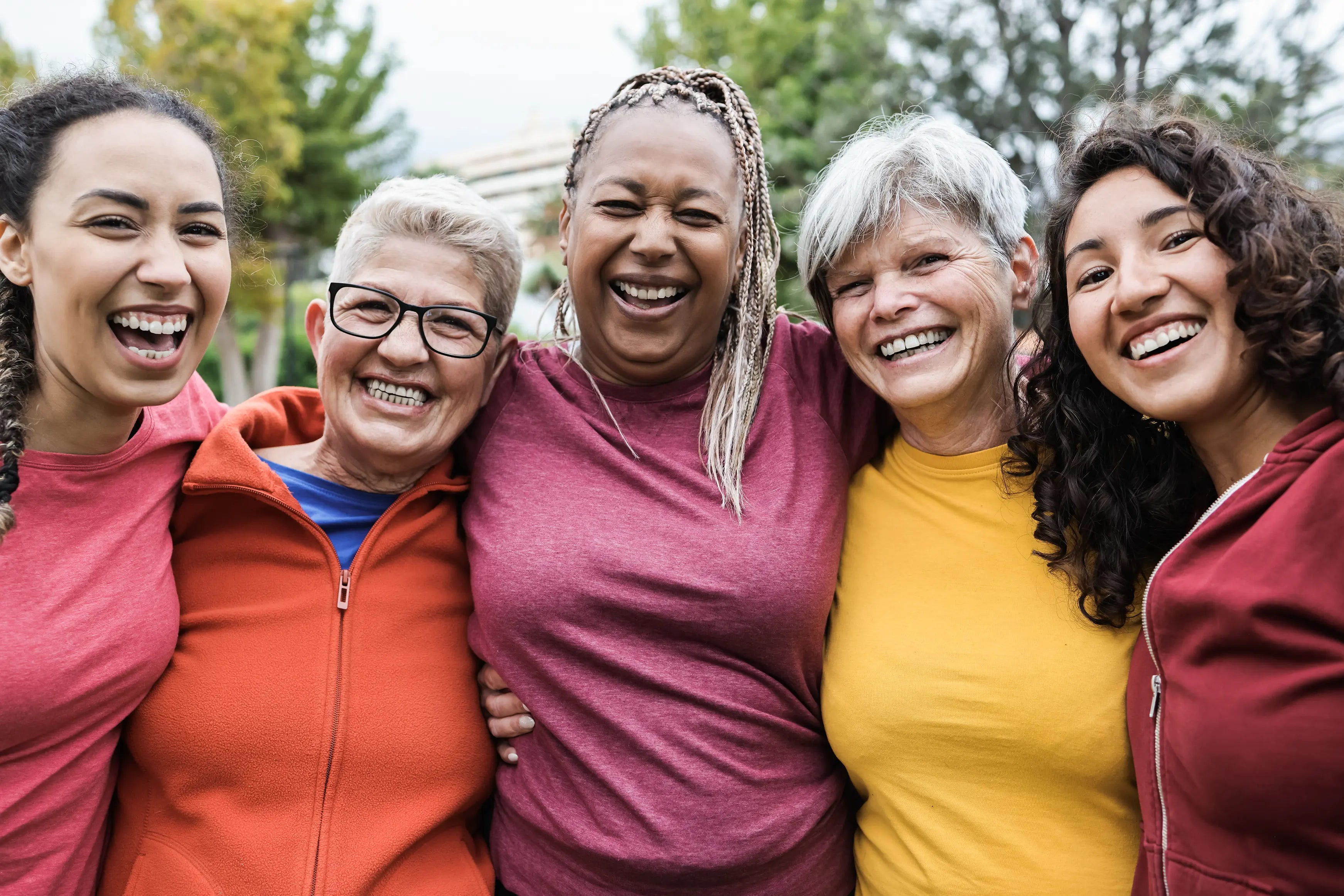 “Smiling diverse group of women of different ages standing close together outdoors with their arms around each other, representing support and community during perimenopause