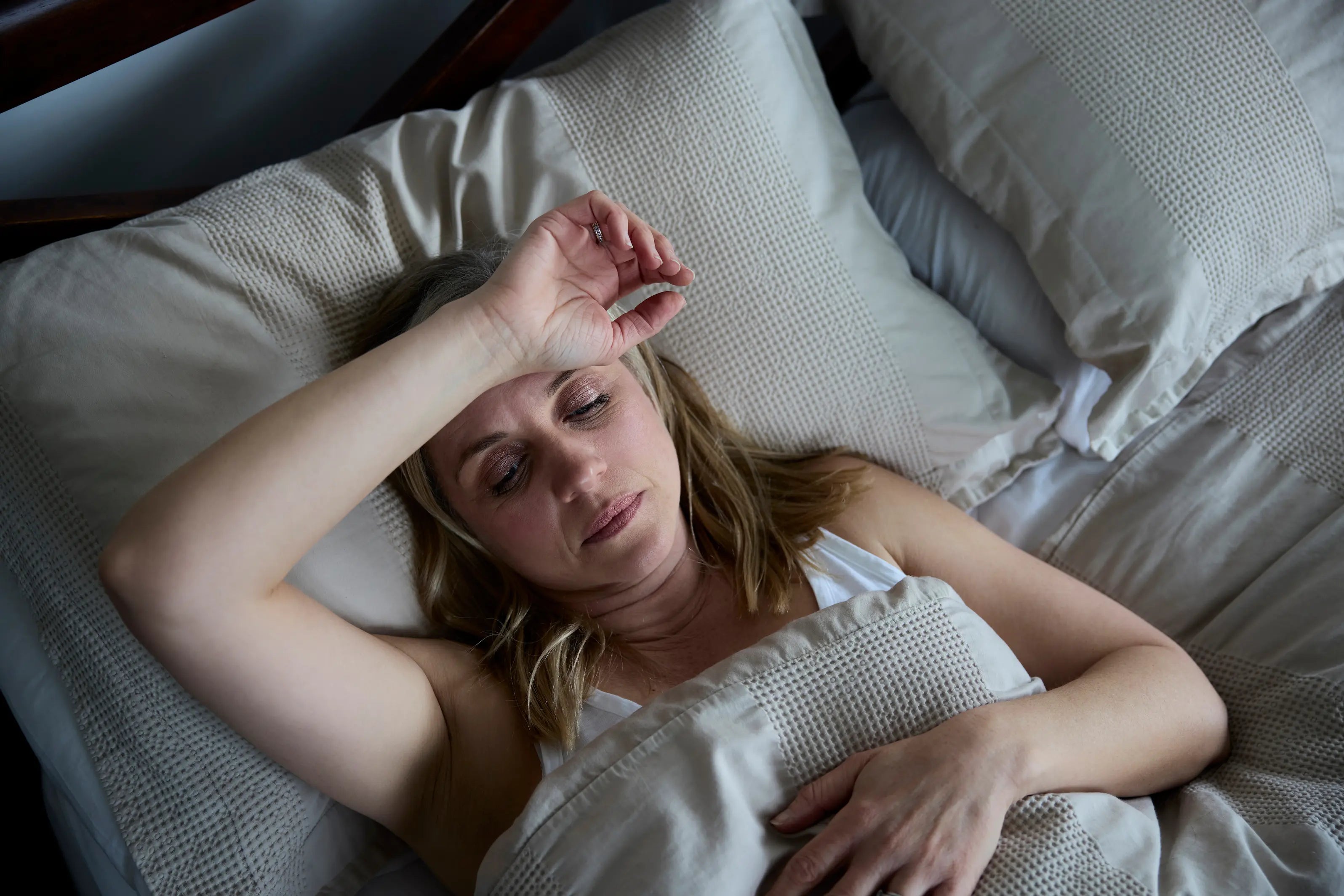 Woman lying in bed unable to sleep, visibly uncomfortable and overheated, representing night sweats and hot flash sleep disruption during perimenopause