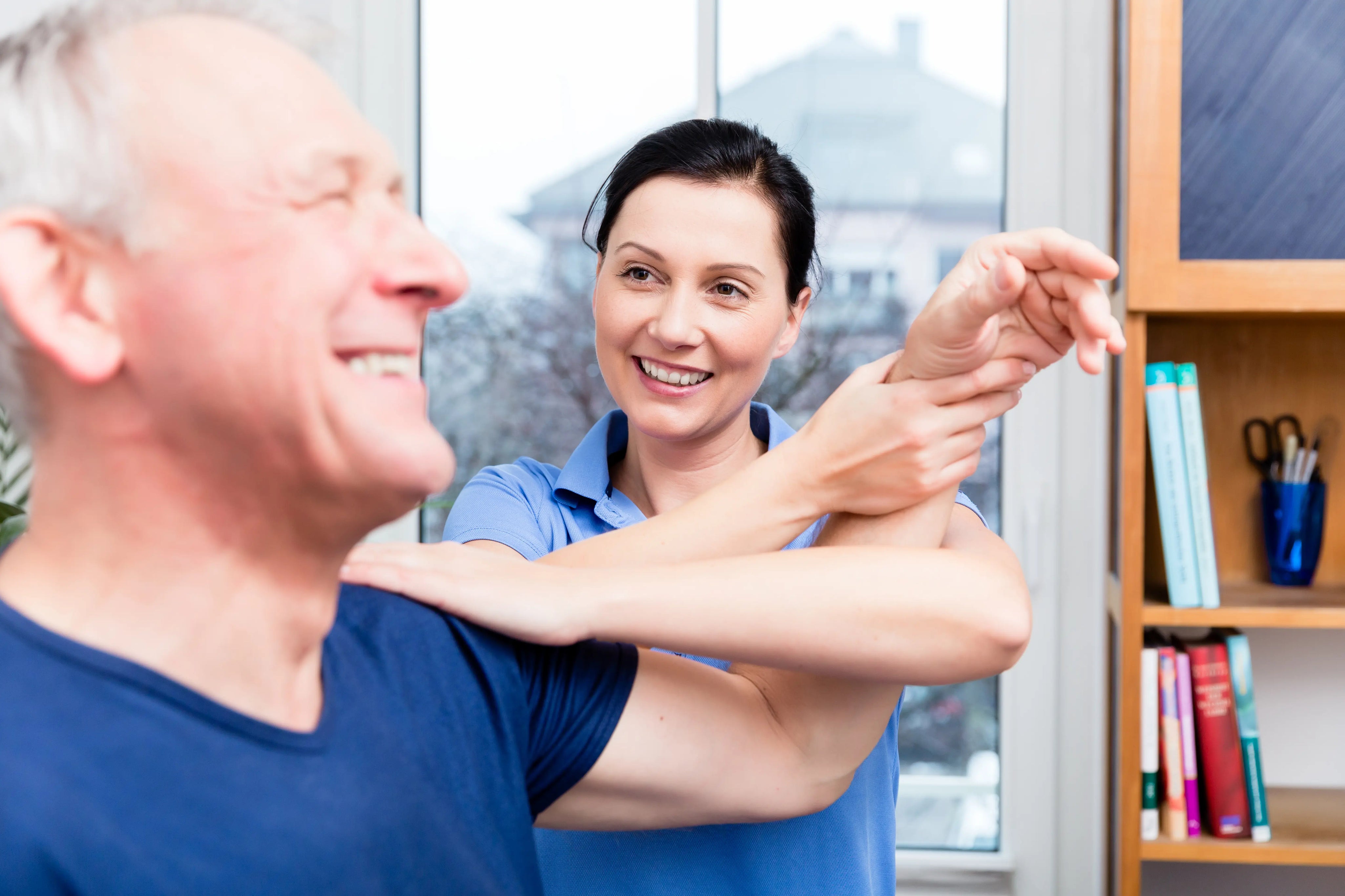 Physical therapist assisting an older man with shoulder and arm mobility exercises during rehabilitation session