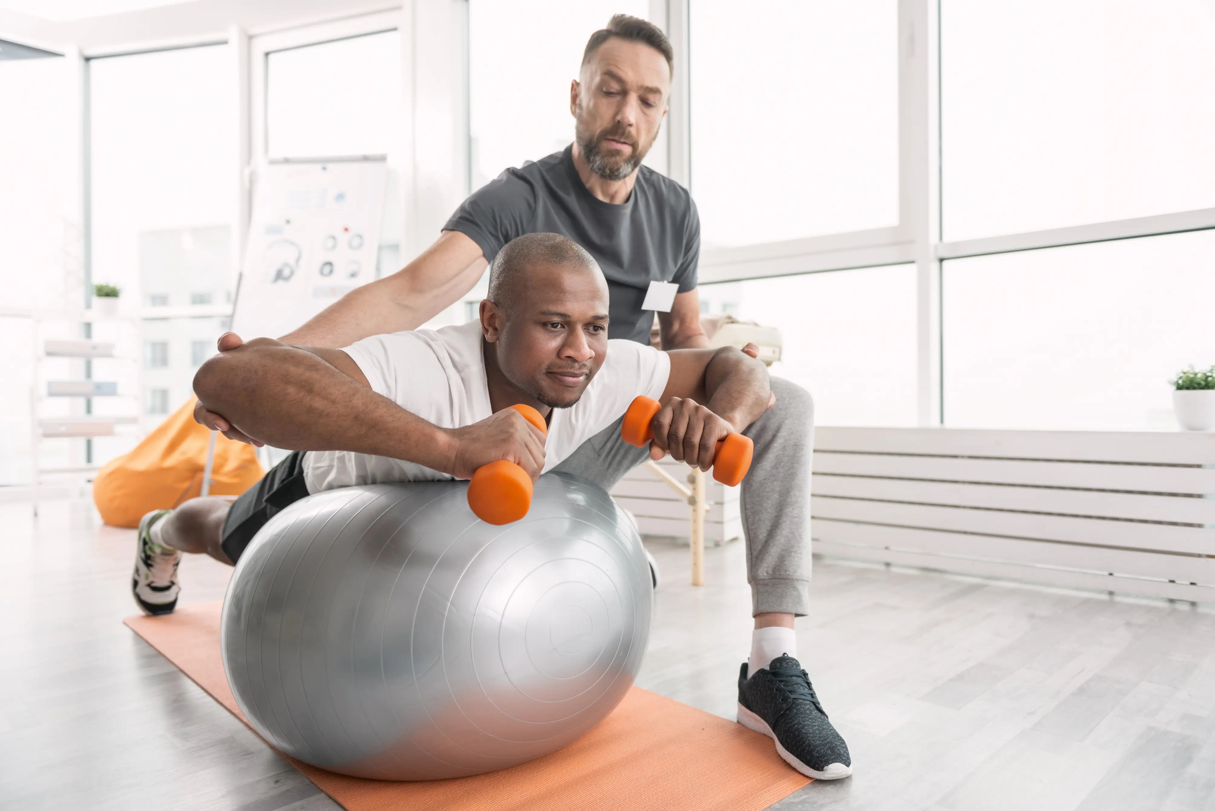 Physical therapist guiding patient through stability ball exercise with dumbbells during rehabilitation session