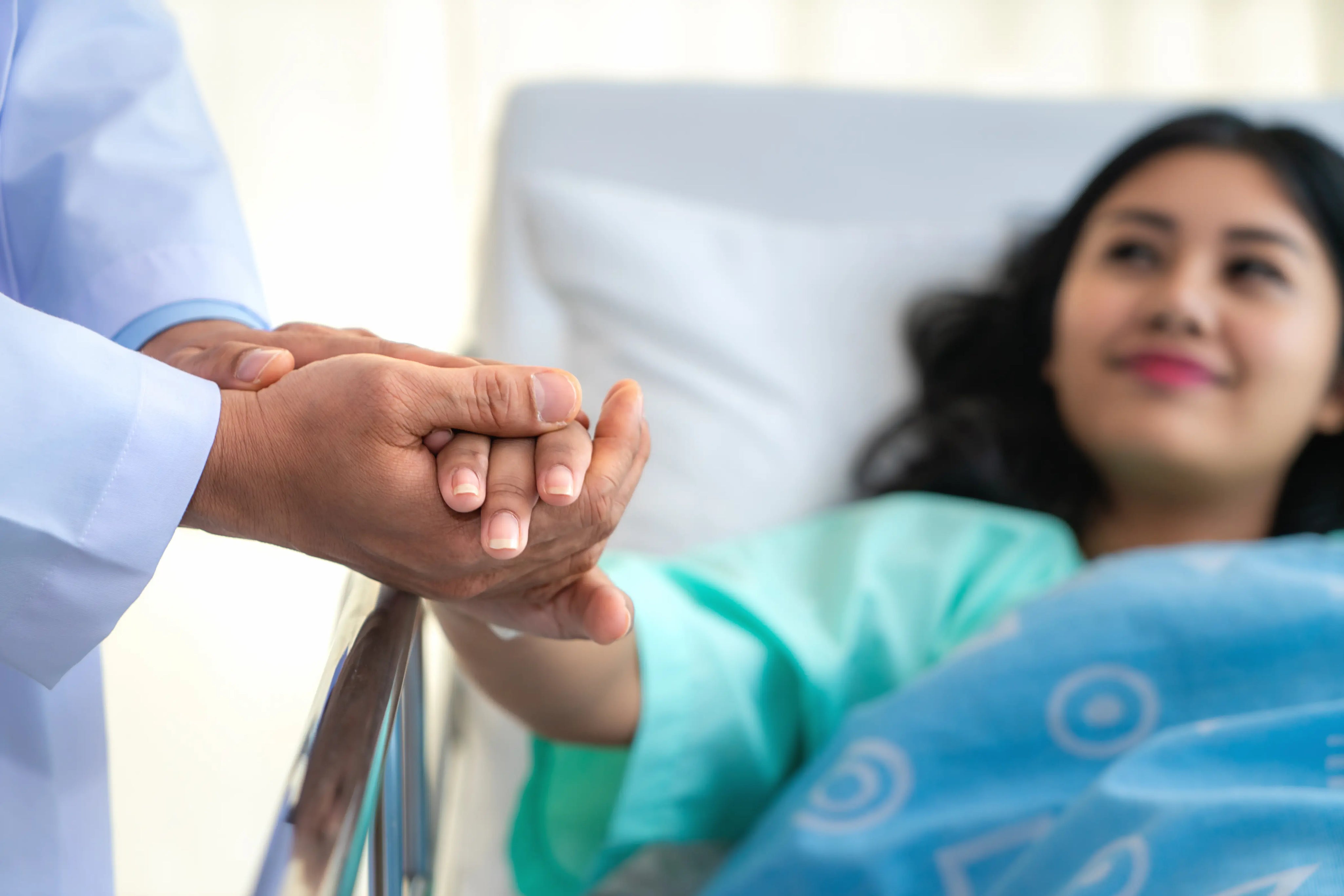 Doctor holding a patient’s hand in a hospital bed, offering comfort and reassurance during recovery.