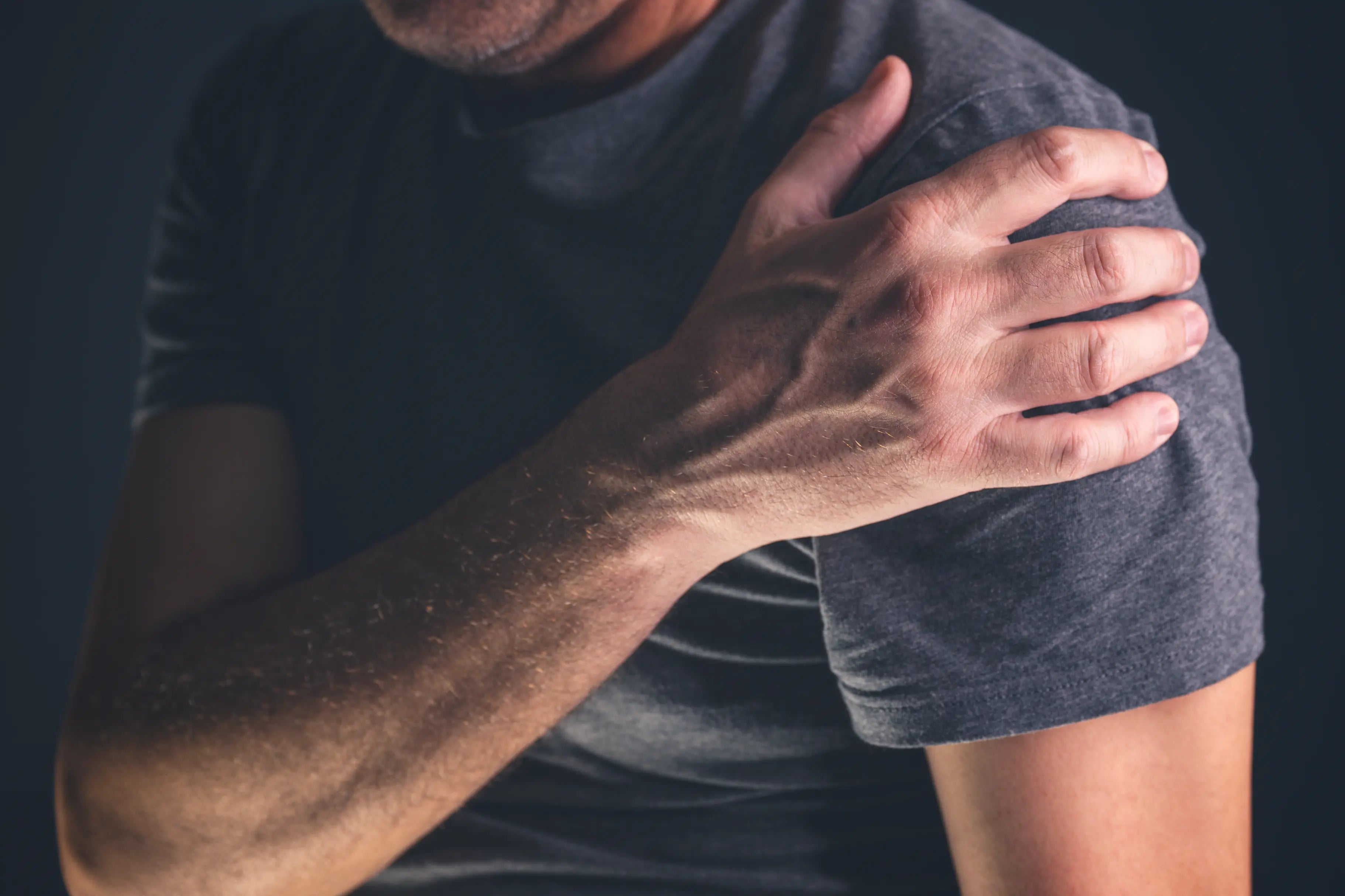 Man holding his shoulder in pain, illustrating rotator cuff injury or post-surgery shoulder discomfort