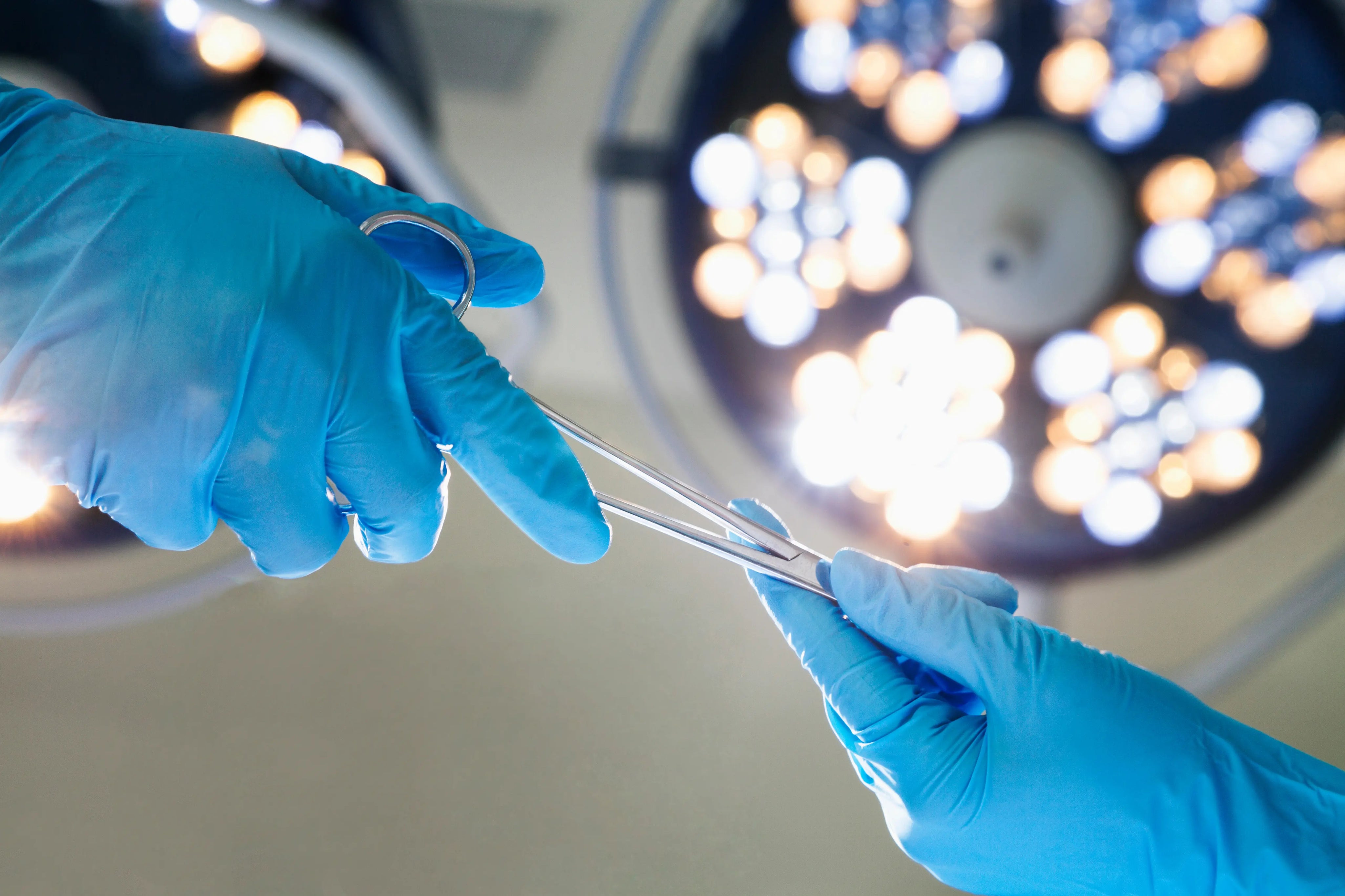 Surgeon’s gloved hands holding surgical instruments under operating room lights during a medical procedure