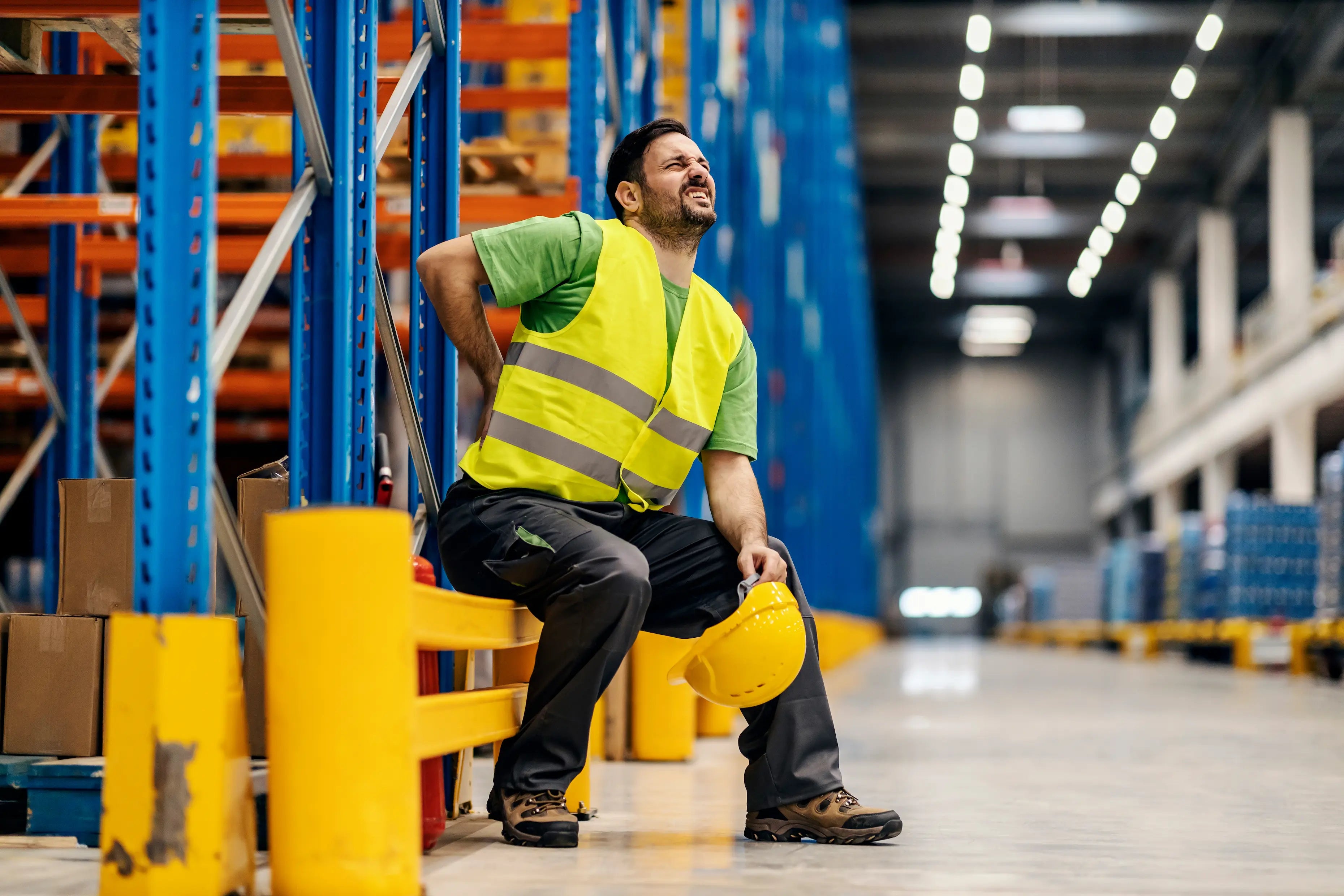 Warehouse worker sitting and holding lower back in pain after lifting injury