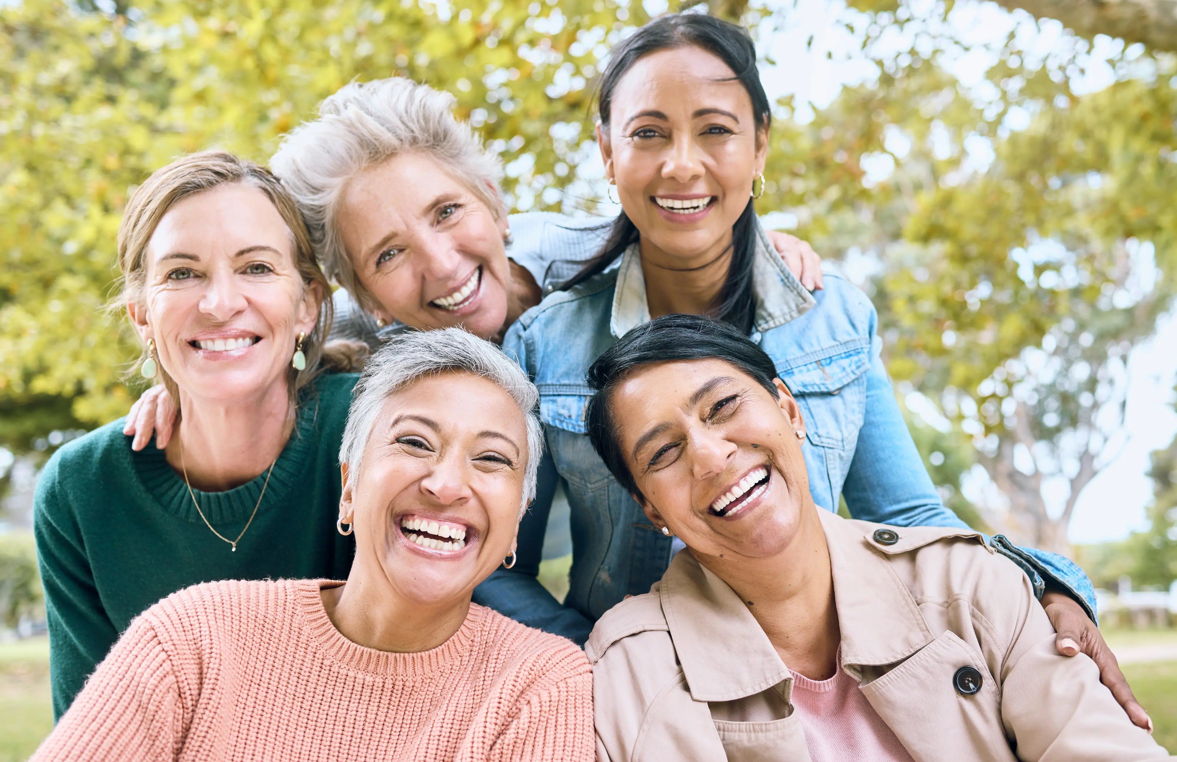 Five diverse women in their 40s and 50s laughing together outdoors, representing community and wellness during menopause and perimenopause