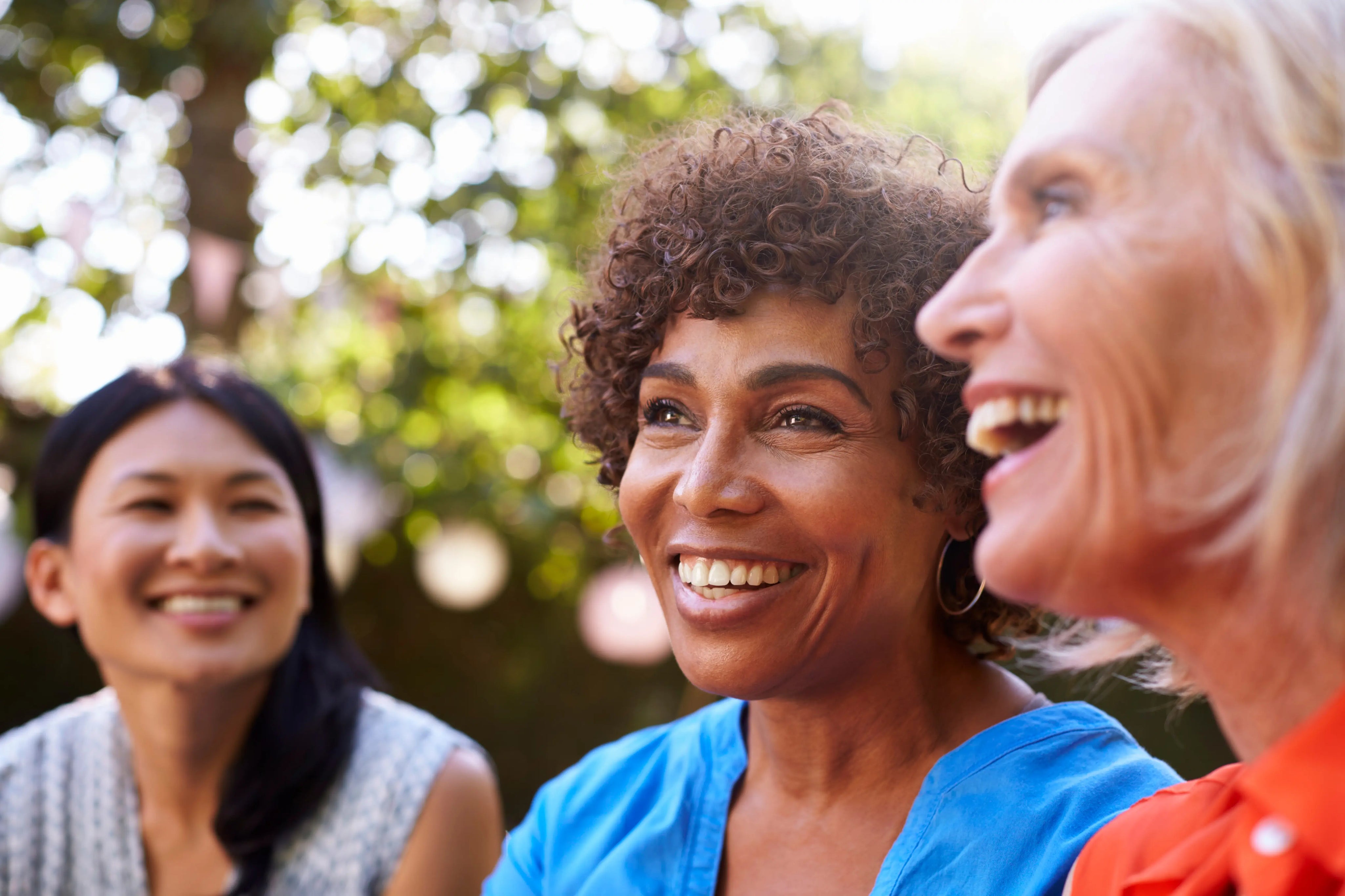 Group of midlife women smiling and talking outdoors, representing support, connection, and wellbeing during menopause.