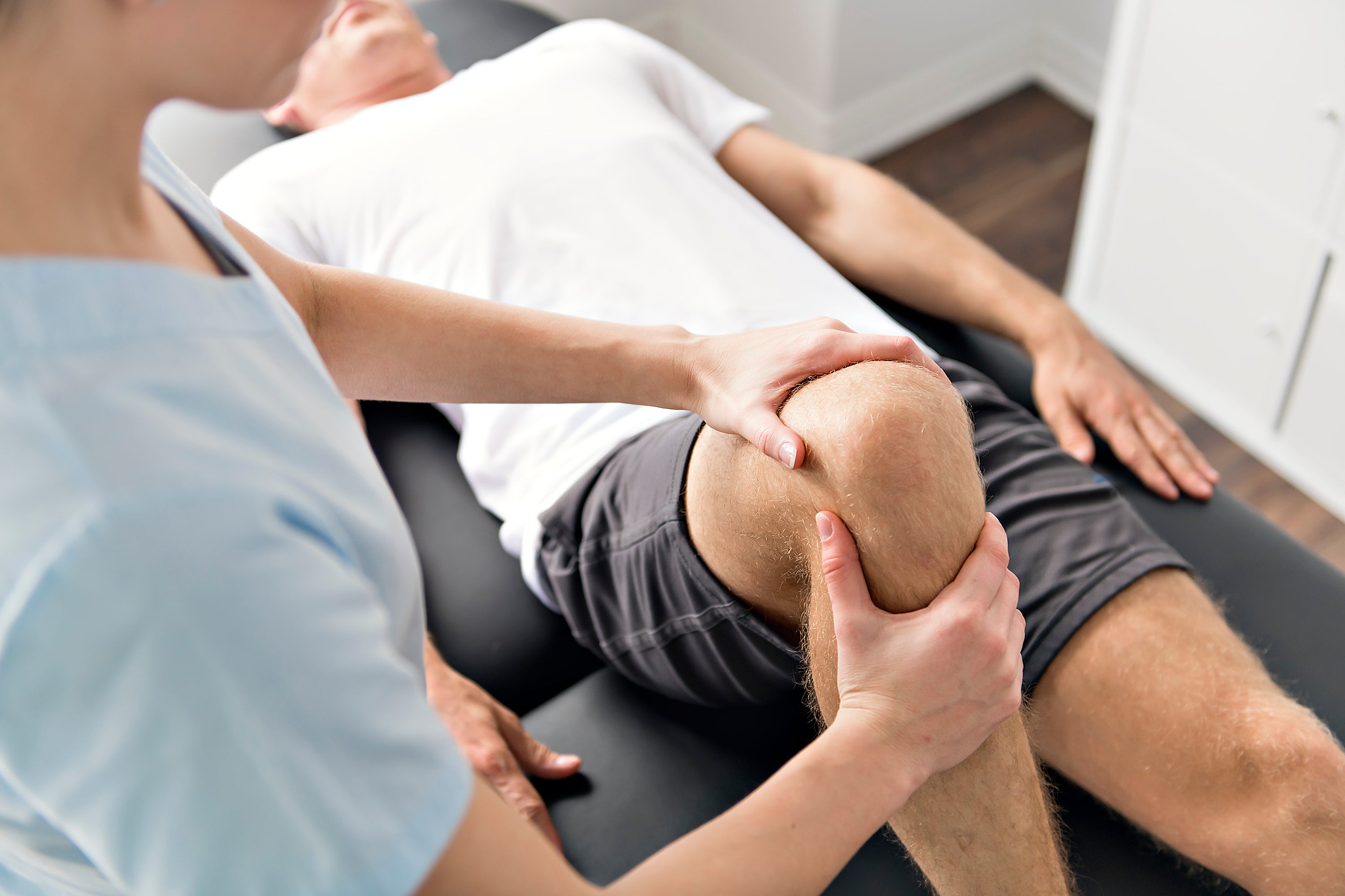 Physical therapist performing a hands-on knee assessment on a patient lying on a treatment table to support joint mobility, injury recovery, and rehabilitation.